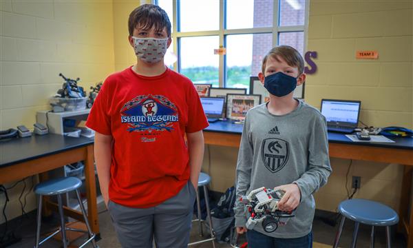 Two boys smile at the camera while holding a robot